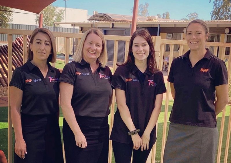 Four women smiling wearing matching collared black shirts standing in a children's play area outside