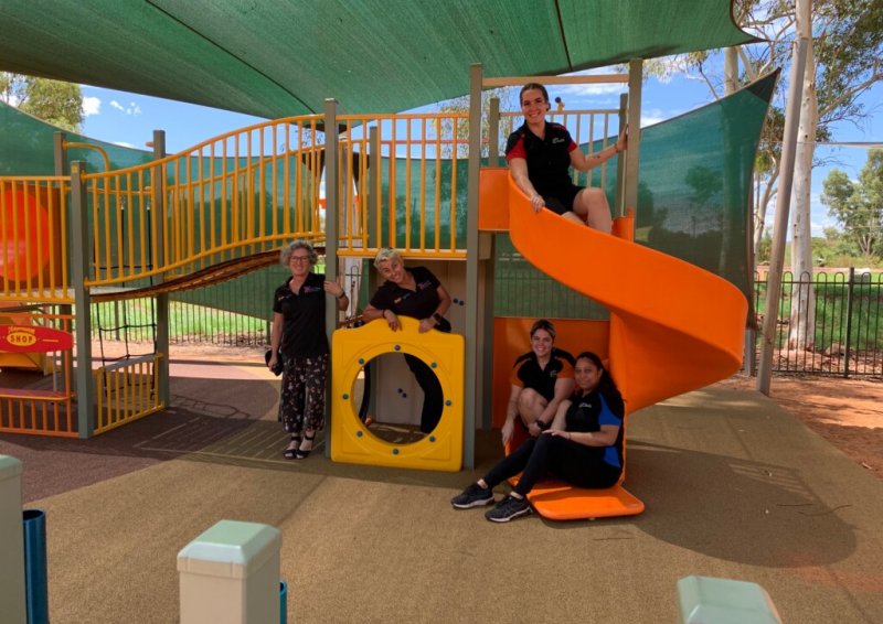 Five staff members variously spaced on children's play equipment